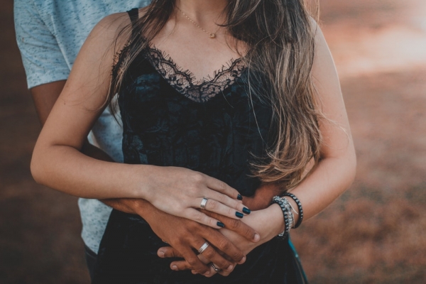 Torso of teenage girl held gently from behind by her boyfriend, hands clasped